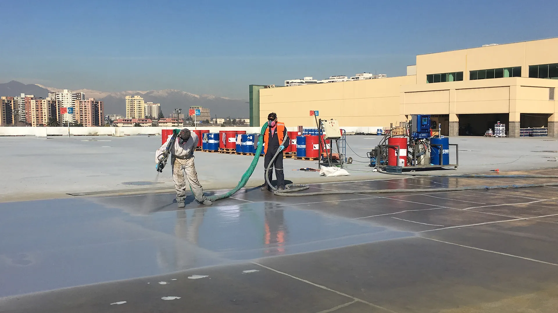 Proyectos Operarios profesionales aplicando recubrimiento de poliurea industrial en una superficie de gran extensión con equipo especializado, destacando la precisión técnica y el uso de elementos de protección personal en una obra de ingeniería a cielo abierto.